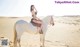 A woman in a bikini riding a white horse in the desert.