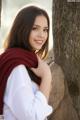 A woman wearing a red scarf leaning against a tree.