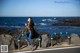 A woman sitting on the side of a road next to the ocean.