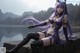 A woman with long purple hair sitting on a wall by the water.