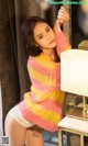 A woman in a pink and yellow sweater leaning against a wall.